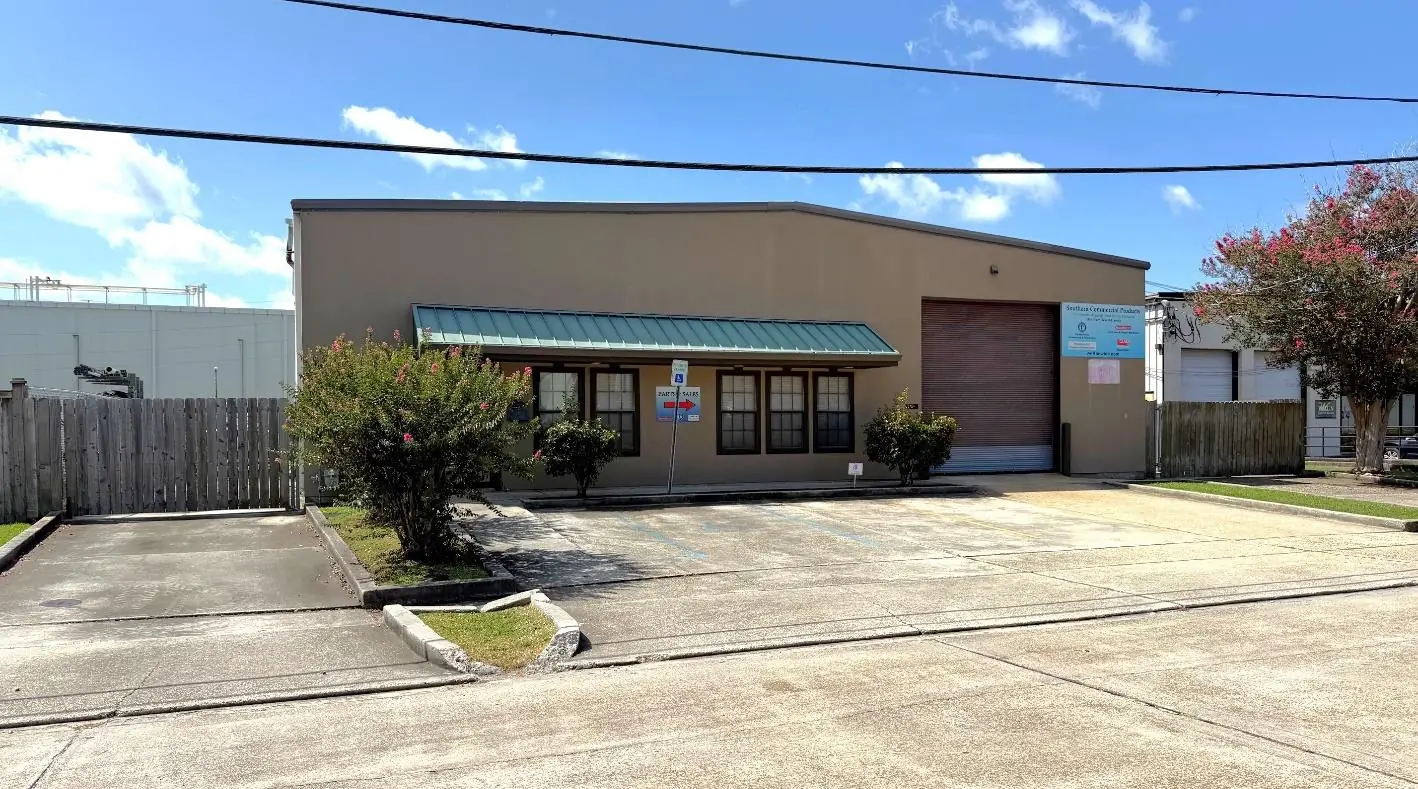 Front of the single-story office/warehouse building with green metal awning, concrete driveway and overhead door